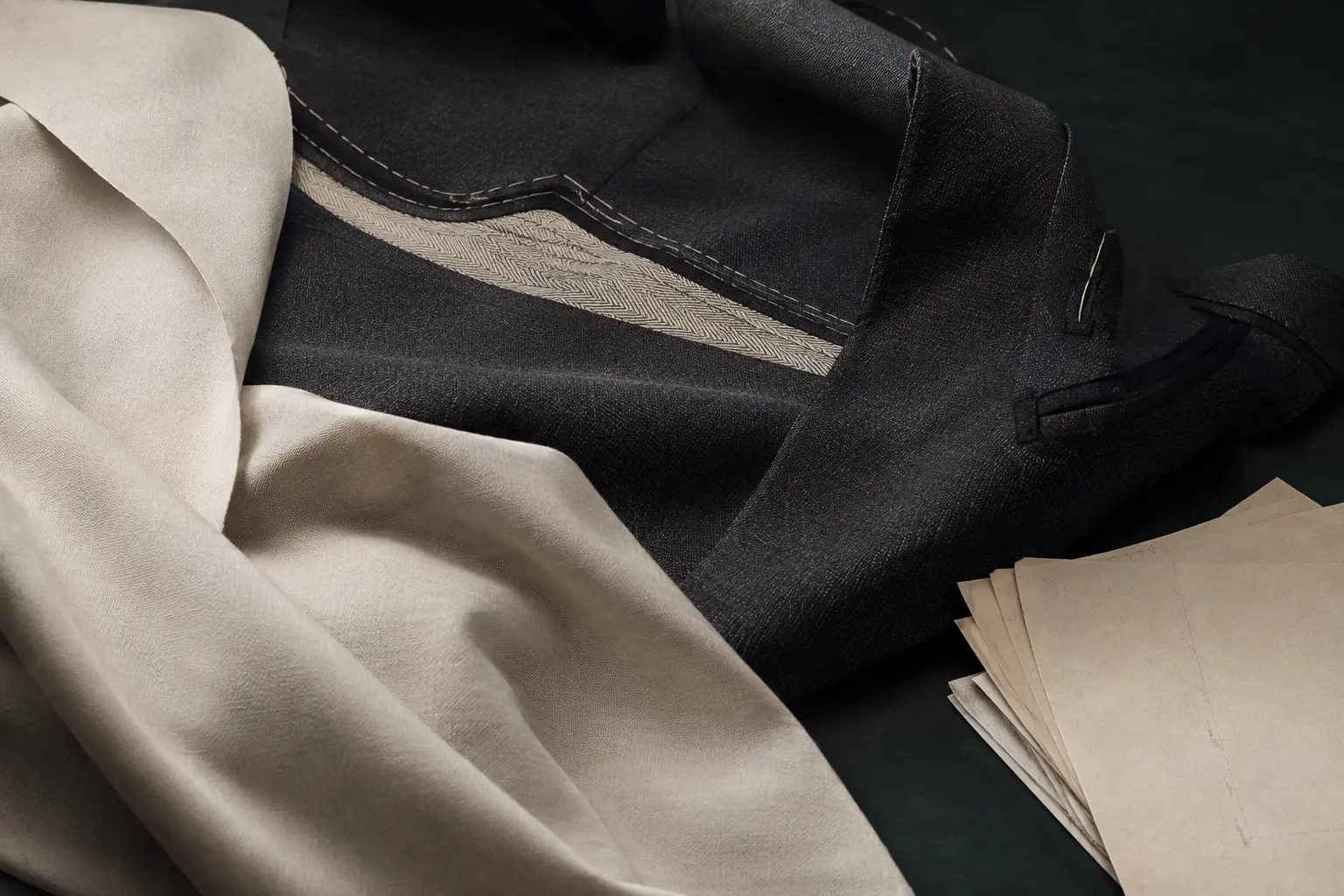 A considered menswear material study with dark tailoring cloth, ivory fabric and pattern paper